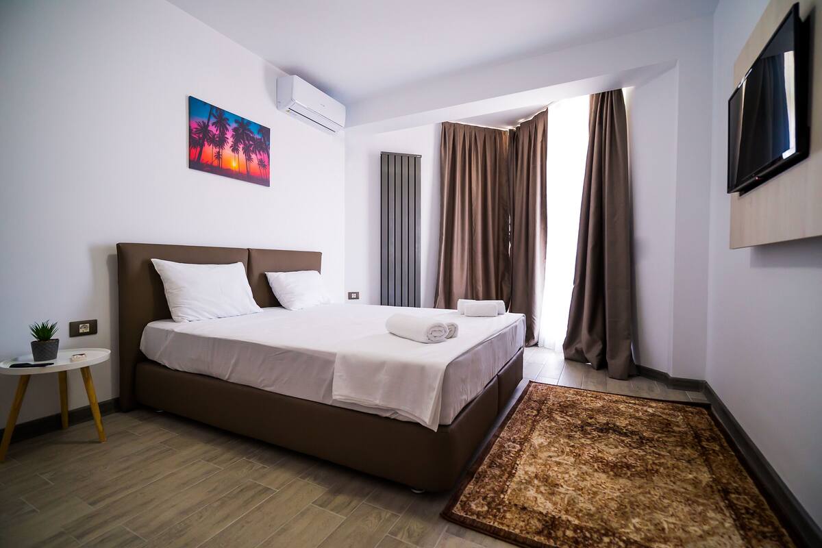 Una habitación de hotel con una cama grande, una mesita con una planta, un televisor de pantalla plana y un cuadro en la pared.