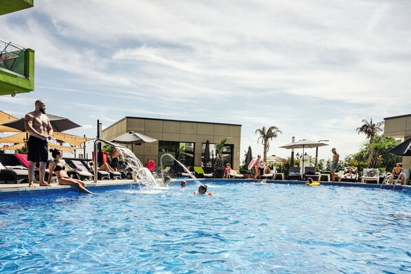 A swimming pool with people, sun loungers, and umbrellas.