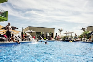 Una piscina con gente, tumbonas y sombrillas.