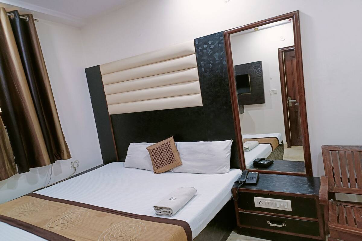 Een hotelkamer met een bed, nachtkastje, spiegel en een houten stoel.