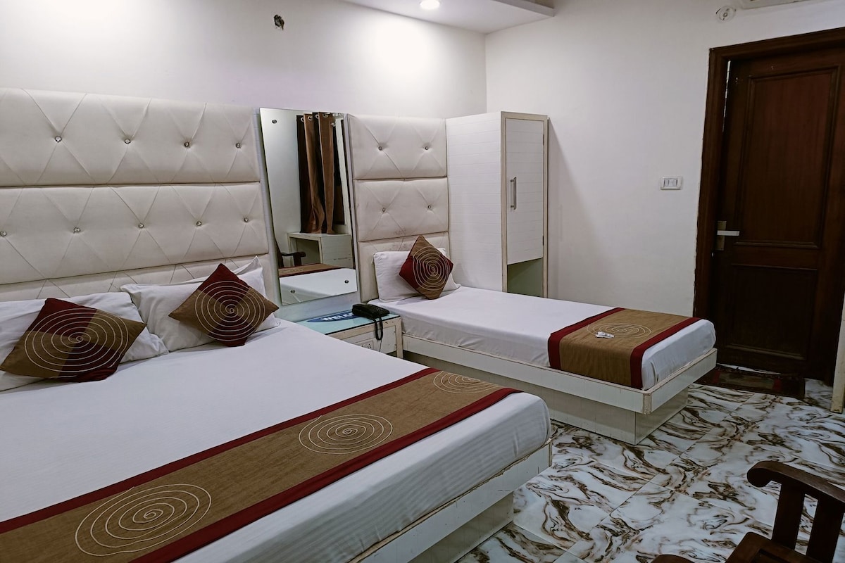 A hotel room with two beds, a wardrobe, a mirror, a bedside table with a phone, and a door.