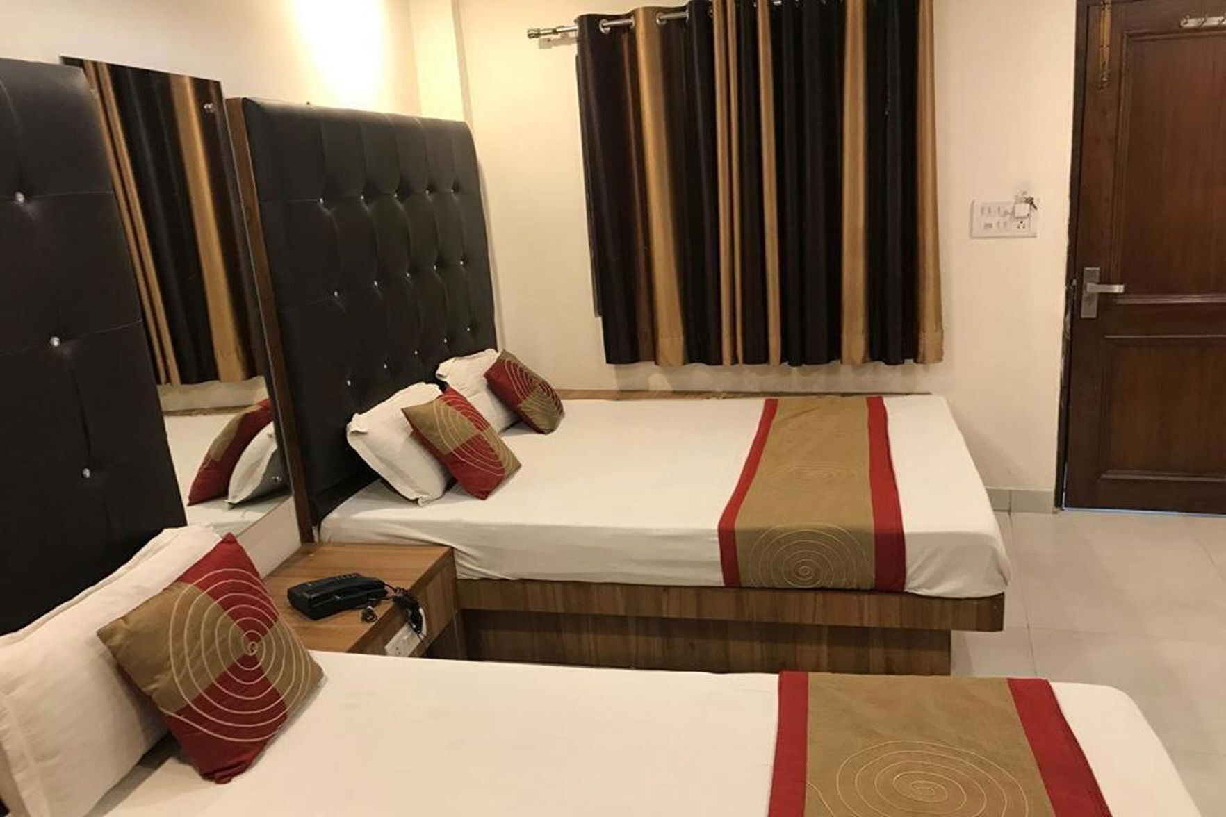 A hotel room with two beds, a wooden headboard, a bedside table with a phone, and a curtain.