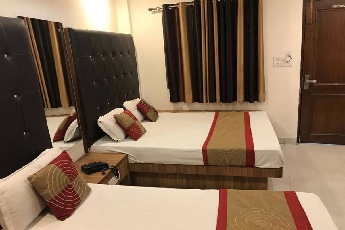 Een hotelkamer met twee bedden, een houten hoofdbord, een nachtkastje met een telefoon en een gordijn.