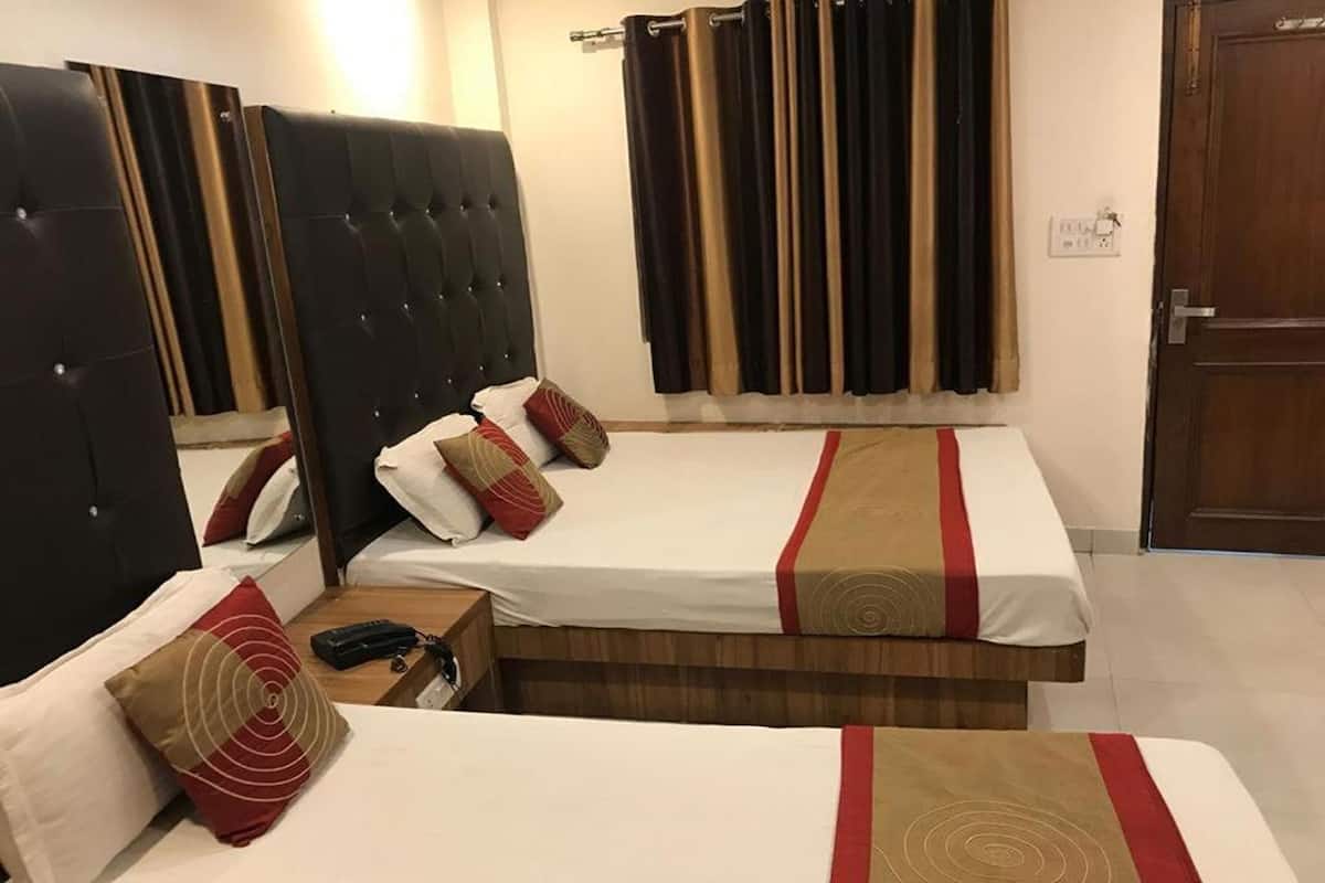 A hotel room with two beds, a wooden headboard, a bedside table with a phone, and a curtain.