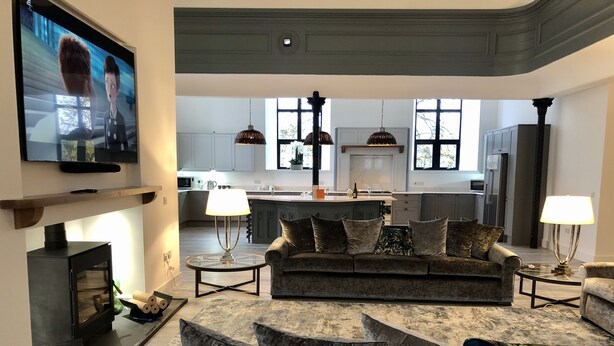 En moderne stue med sofa, fjernsyn, pejs og et køkken i baggrunden.