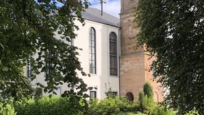 En bygning med et tårn og et ur, en græsplæne med en bænk, og et vandelement.