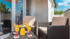 Un balcon agrémenté de meubles en osier, d’une table en verre et d’une carafe en verre remplie de jus d’orange.