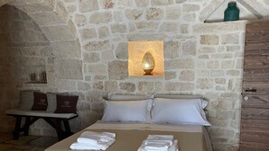 A stone-walled room with a bed, a table with chairs, and a wooden cabinet. - Trullo Valle d'Itria (Martina Franca)