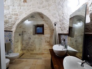 A bathroom with stone walls, a shower, a wooden vanity, and a large mirror.