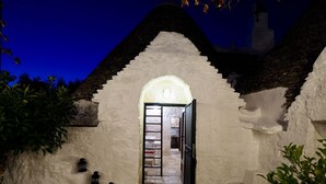 A white-walled building with a stone roof, a doorway leading to an interior space, and a small table with a potted plant. - Trullo Valle d'Itria (Martina Franca)