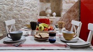 A table set with bread, fruits, a jar of jam, and cups, with a rustic stone wall and a red chair in the background. - Trullo Valle d'Itria (Martina Franca)