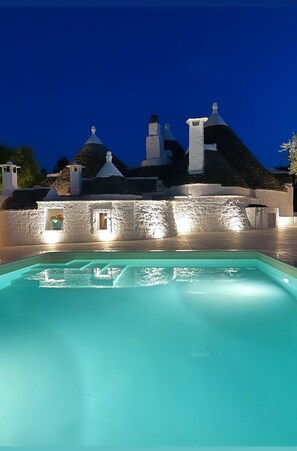 A swimming pool with a stone wall and a building with multiple chimneys in the background.