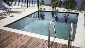 Ein Schwimmbecken mit Holzterrasse und Metallgeländern, umgeben von einem Zaun und Pflanzen.