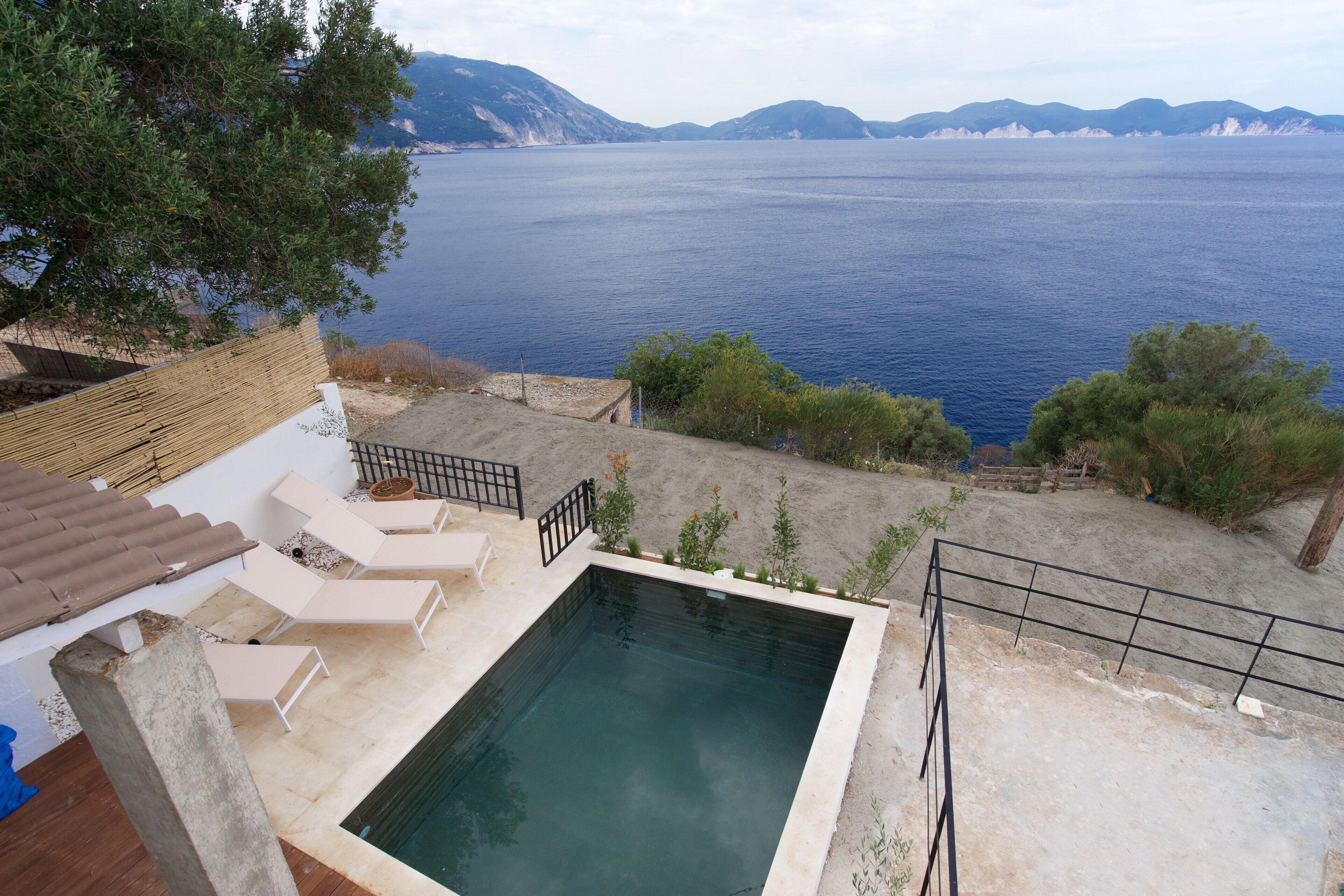 A swimming pool with lounge chairs, a view of the sea, and mountains in the background.