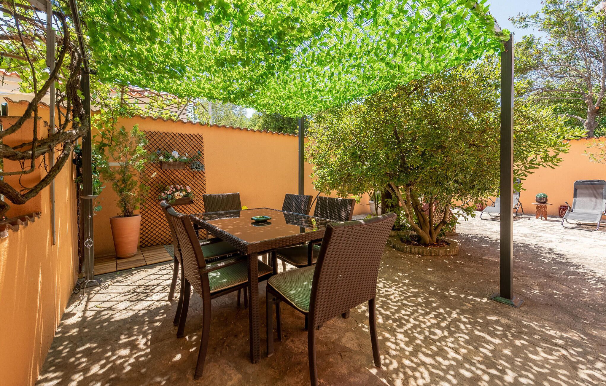 A patio with a table and chairs, surrounded by plants and a fence.