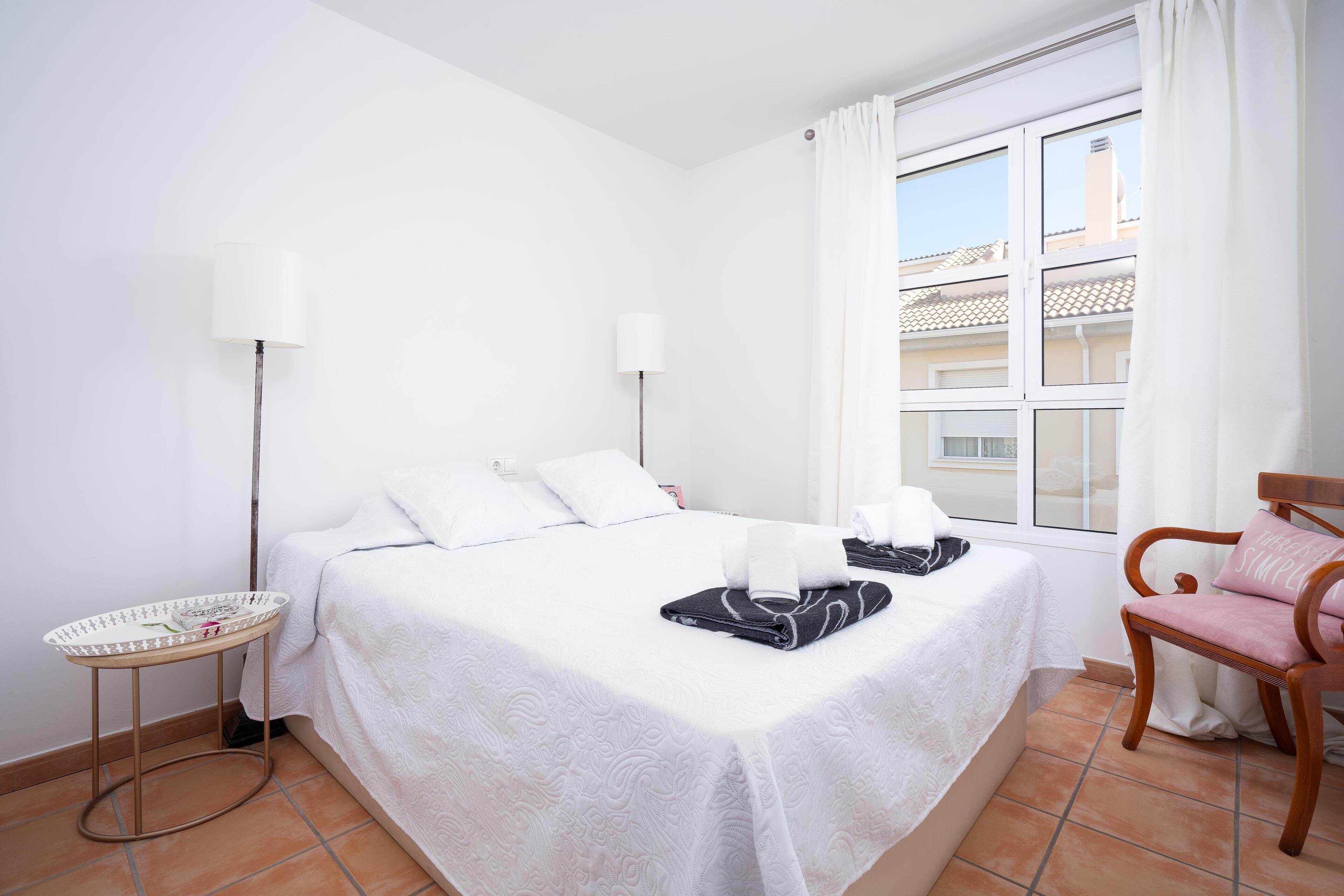 Une chambre d’hôtel avec un grand lit, deux tables de chevet, une chaise et une fenêtre avec des rideaux.