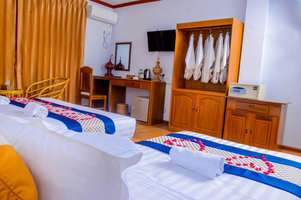 A hotel room with two beds, a desk with a computer, a television, and a wardrobe with hanging clothes.