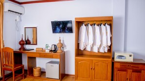 A room with a wooden desk, a chair, a small refrigerator, a television, a mirror, a cabinet with hanging robes, and a small cabinet with a radio. - City Light Hotel (Nyaungshwe)