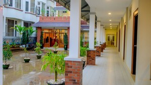 A corridor with potted plants, brick pillars, and a building entrance with a glass door. - City Light Hotel (Nyaungshwe)