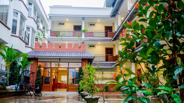 A courtyard with potted plants, a seating area, and a building with multiple floors and balconies. - City Light Hotel (Nyaungshwe)