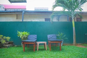 A small outdoor seating area with two chairs and a stool, surrounded by a green wall and a palm tree. - Hasaranga Holiday House (Hikkaduwa)
