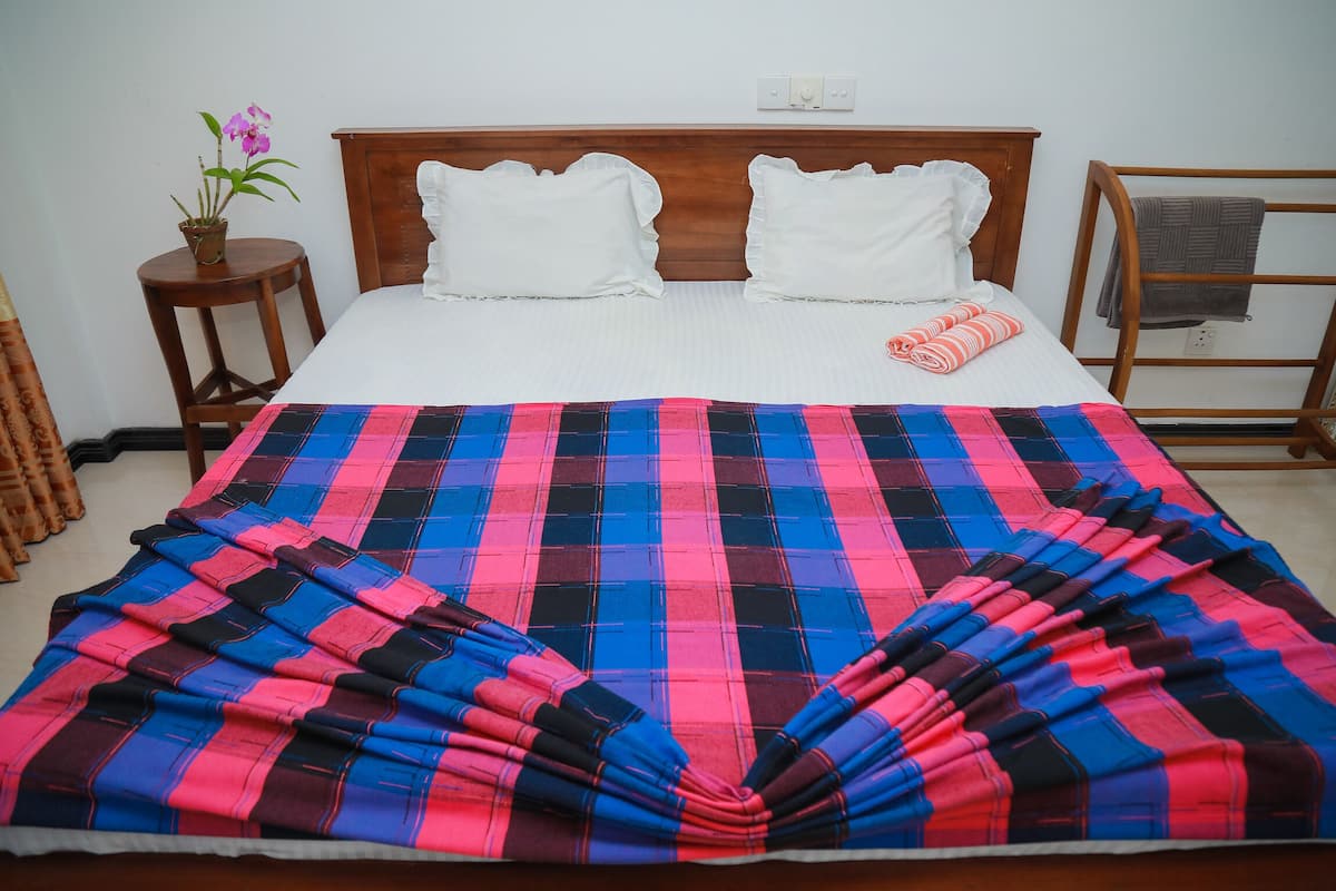 A neatly made bed with a plaid blanket, white pillows, and a small potted plant on a wooden nightstand.