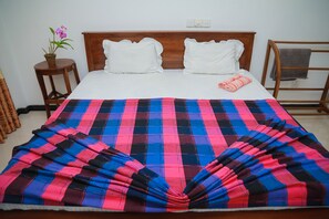 A neatly made bed with a plaid blanket, white pillows, and a small potted plant on a wooden nightstand. - Hasaranga Holiday House (Hikkaduwa)