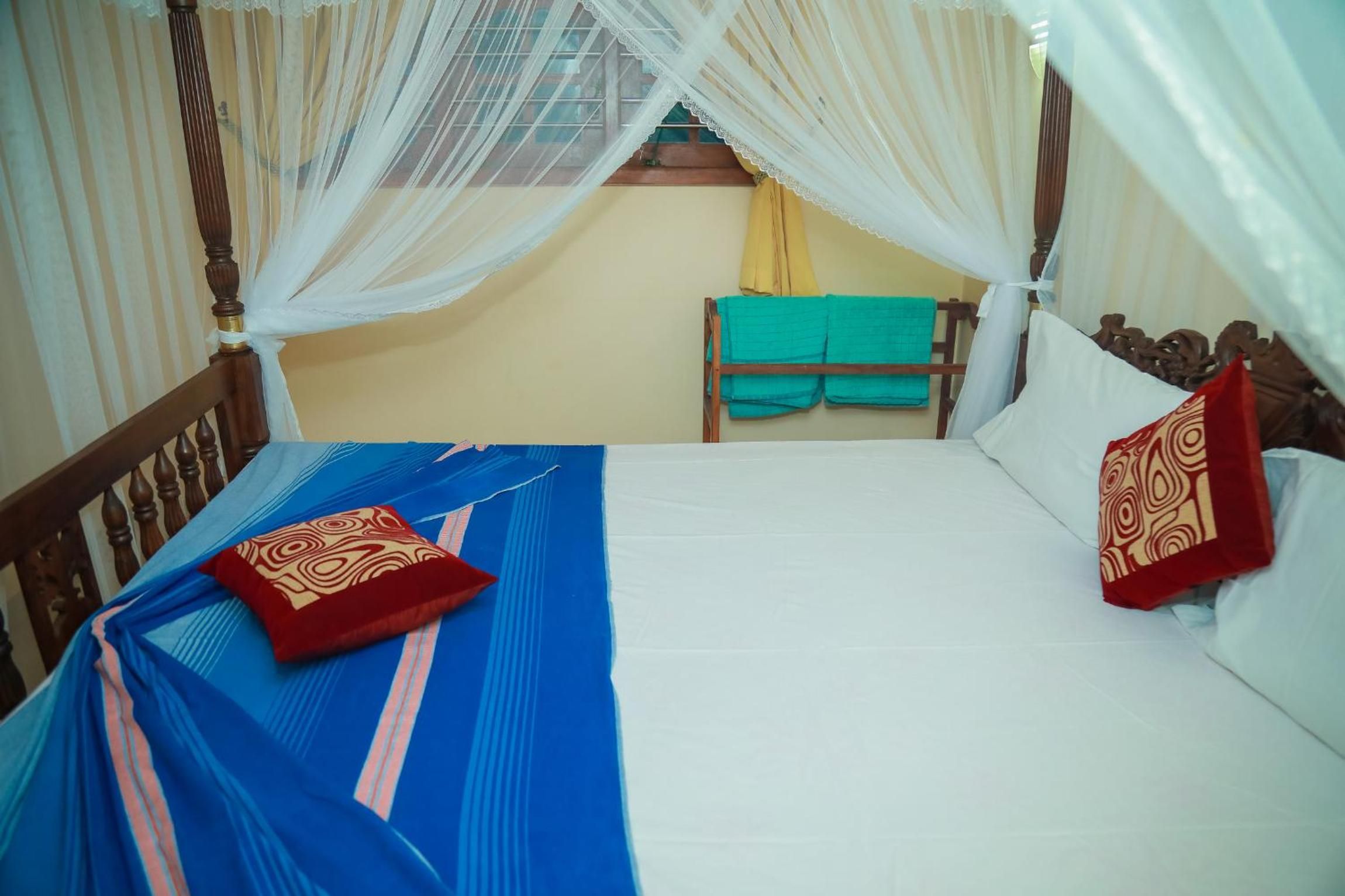 A bed with a blue bedspread and two pillows, a wooden headboard, and a canopy with sheer curtains.