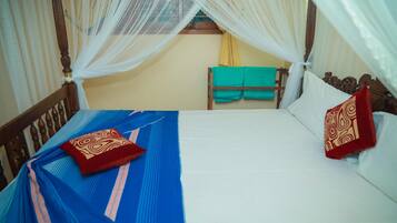 A bed with a blue bedspread and two pillows, a wooden headboard, and a canopy with sheer curtains.