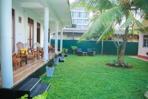 A covered outdoor seating area with wooden chairs and tables, surrounded by potted plants and a well-maintained lawn. - Hasaranga Holiday House (Hikkaduwa)