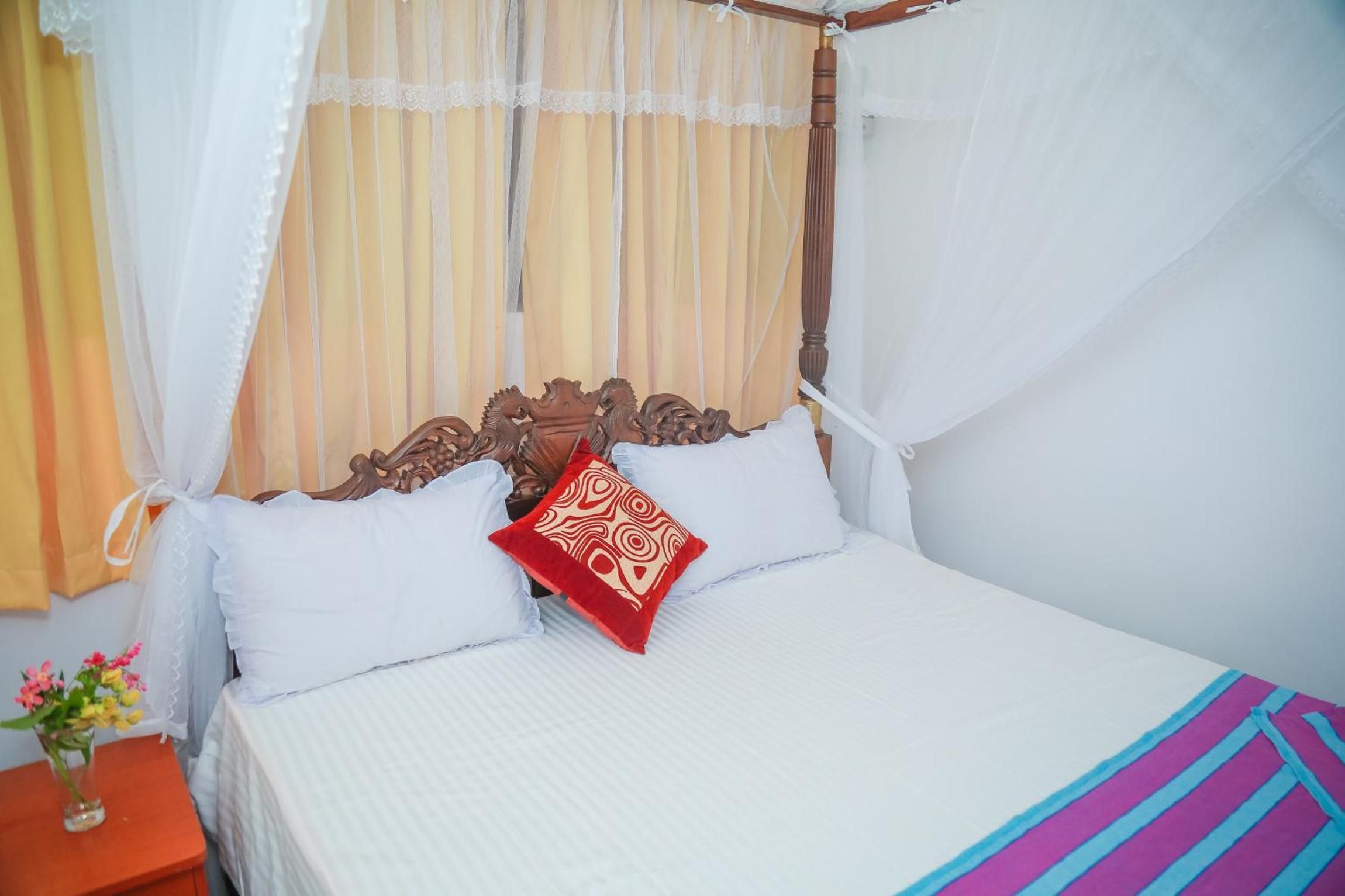 A bed with a canopy, white bedding, and a single red pillow.