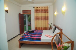 A bedroom with a bed, a wooden headboard, a bench, a potted plant, and a window with curtains. - Hasaranga Holiday House (Hikkaduwa)