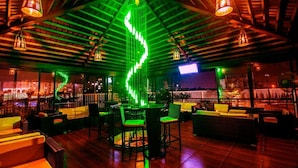 Un bar en la azotea con una instalación de luces de neón verde, vigas de madera y mesas al aire libre.
