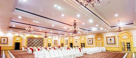 A large banquet hall with rows of tables set for a formal event, chandeliers, and a patterned carpet.