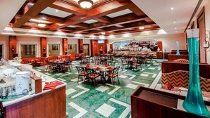 Un amplio vestíbulo de hotel con varias zonas de comedor, un bar central y una gran lámpara de araña.