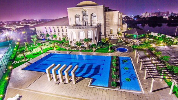 Un hotel con una piscina grande, un área techada y vistas de la ciudad de noche.