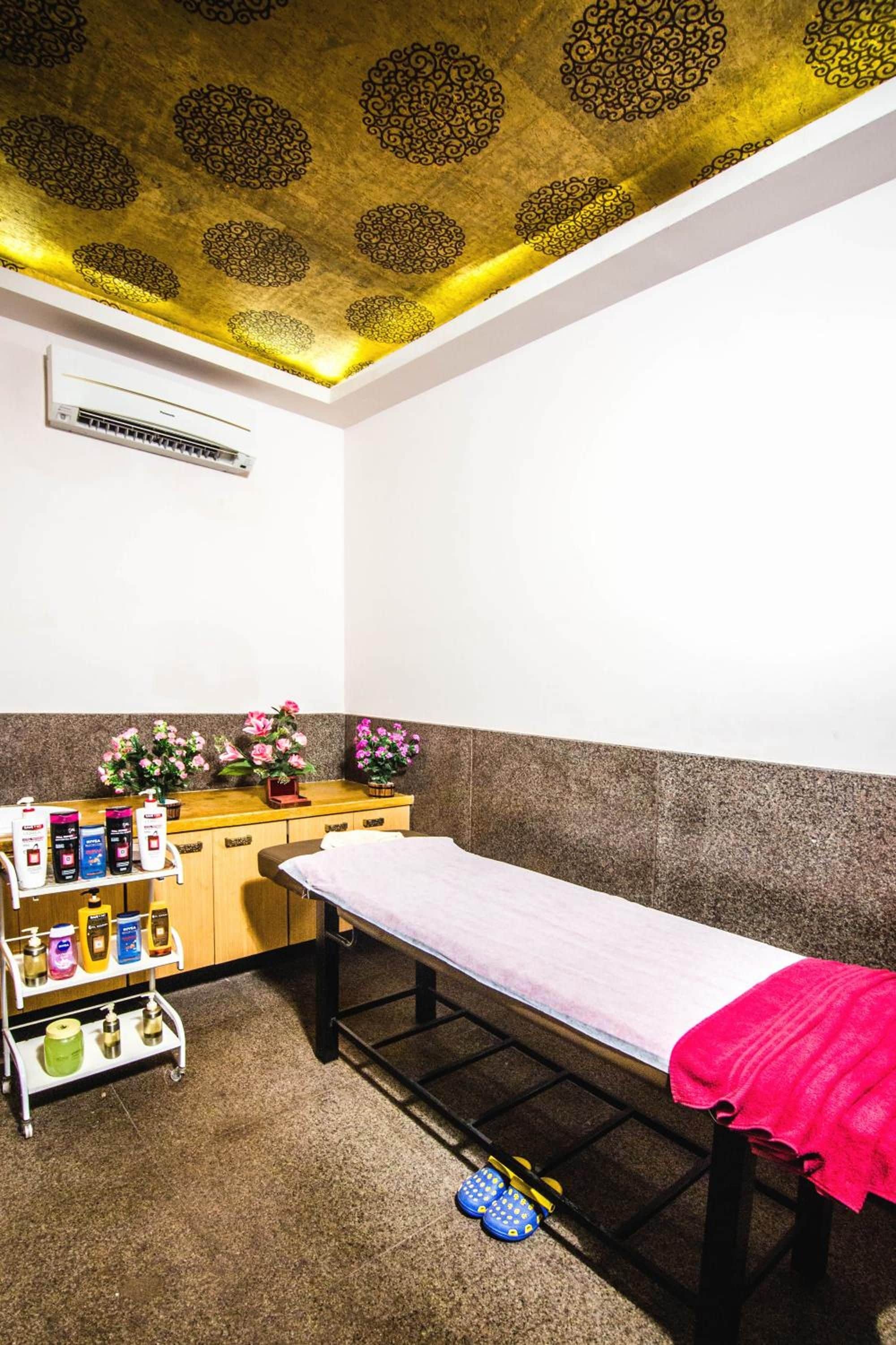 A room with a bed, a small table with toiletries, and a ceiling with a decorative pattern.