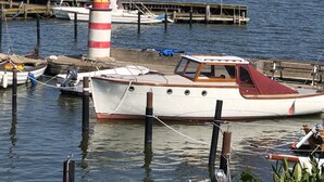 Ein Yachthafen mit vertäuten Booten, einem Leuchtturm und einem Segelboot in der Ferne.