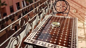 Un balcon agrémenté d’une table et de chaises à motifs, donnant sur un immeuble doté de nombreux balcons et bordé de palmiers.
