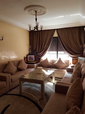 A living room with a beige sofa set, a glass coffee table, and a chandelier.