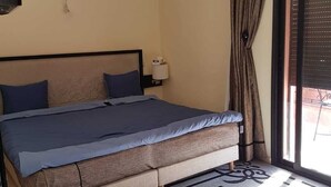 Une chambre à coucher comprenant un lit, une table de chevet, une lampe, une fenêtre avec des rideaux et un ventilateur de plafond.