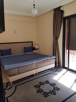 A bedroom with a bed, a nightstand, a lamp, a window with curtains, and a ceiling fan. - Residence Fatine Gueliz Marrakech (Marrakesh)