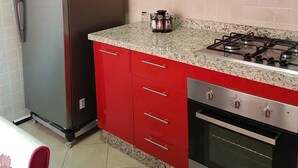 Une cuisine avec des meubles de couleur rouge, un réfrigérateur en acier inoxydable, une cuisinière à gaz et un four encastré.