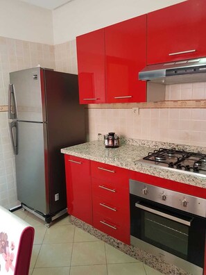 A kitchen with red cabinets, a stainless steel refrigerator, a gas stove, and a built-in oven.