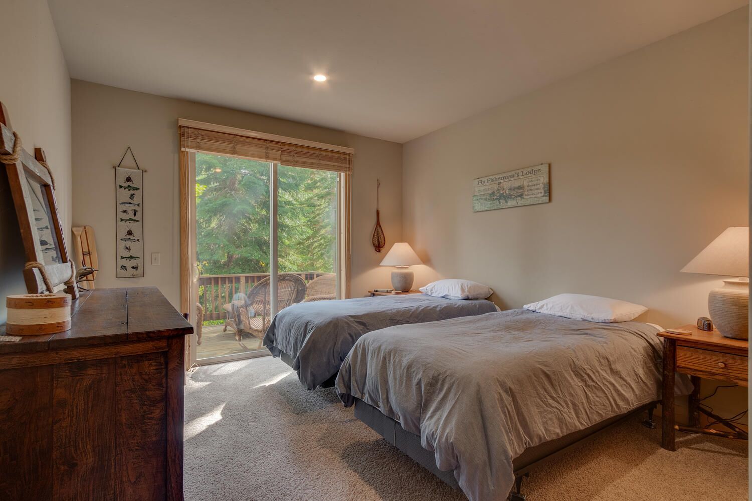 A bedroom with two beds, a wooden dresser, a desk, and a window with blinds.
