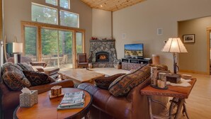 Amplia sala de estar con chimenea de piedra, sofás de cuero y un televisor grande.