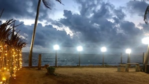 A beach with a sandy shore, palm trees, and string lights. - C J Beach Resort (Uswetakeiyawa)