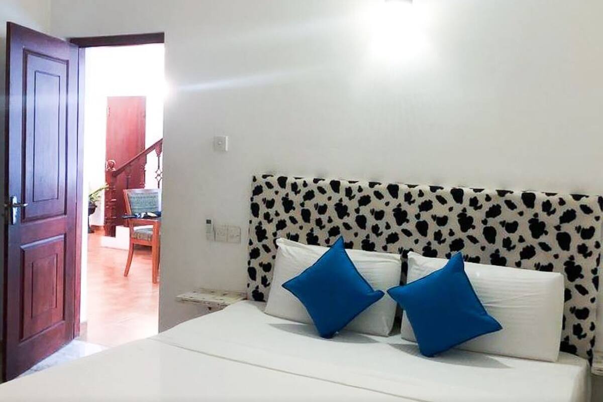 A bedroom with a bed, a headboard with a cow print pattern, and a door leading to another room.