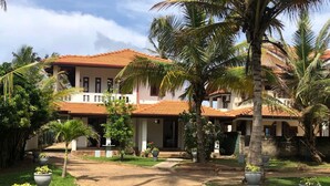 A two-story building with a tiled roof, surrounded by palm trees and potted plants. - C J Beach Resort (Uswetakeiyawa)