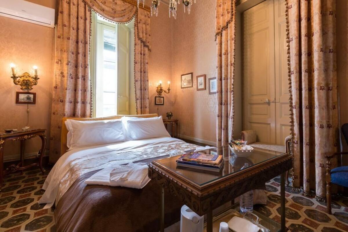 A classic room with a large bed, a glass table, and ornate curtains.